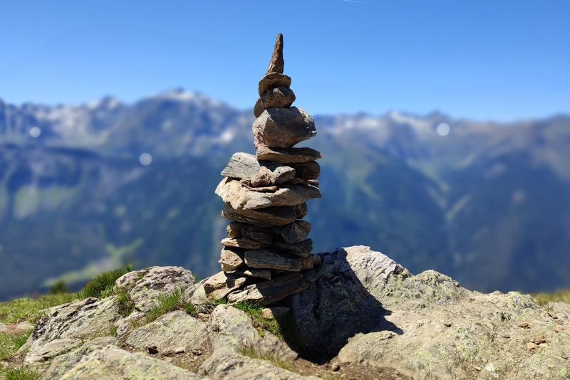 A stack of balanced rocks against a backdrop of mountain ranges and a clear blue sky.